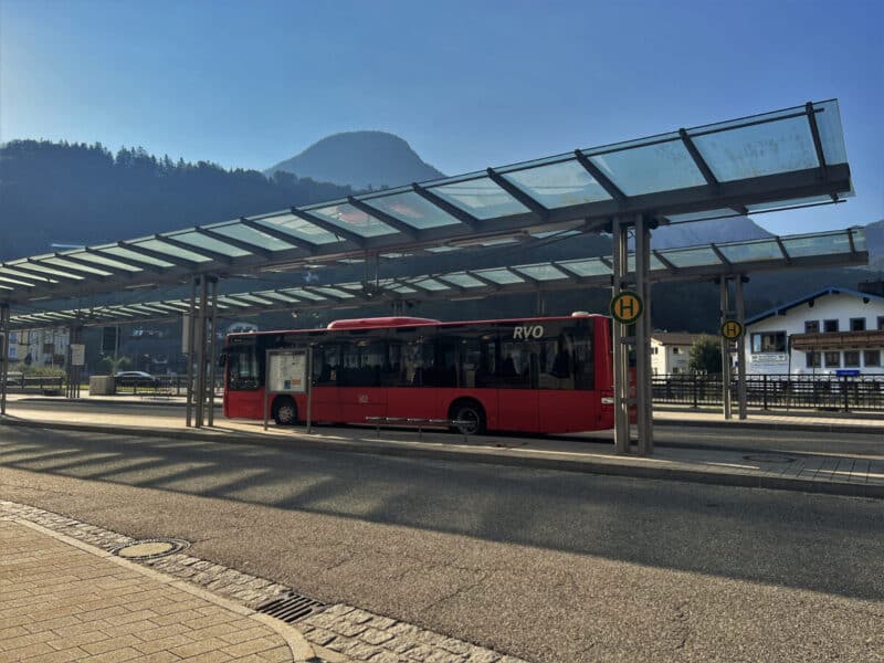Red RVO public bus parked at Berchtesgaden bus station under a glass roof with soft mountain light in the background.