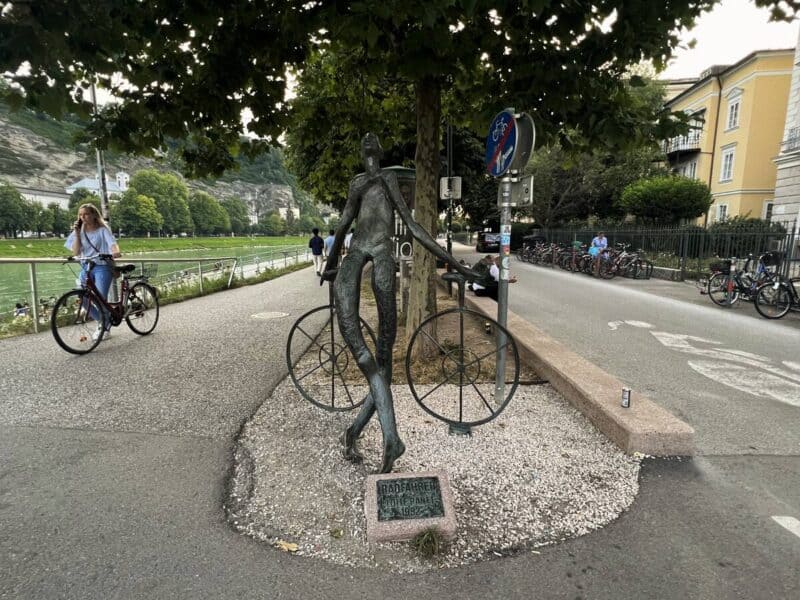 woman on cycle on the move on salzach river bank beside a weird statue