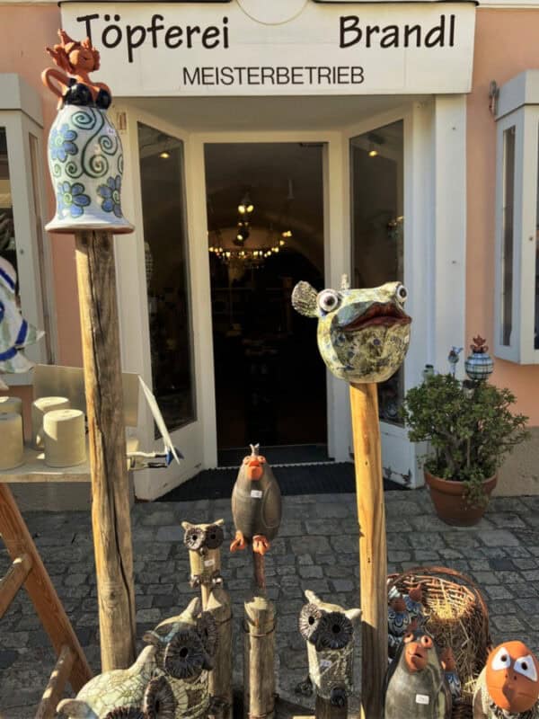 Entrance to Töpferei Brandl pottery shop in Melk, with quirky ceramic animal figures on wooden sticks displayed outside on cobblestone pavement.