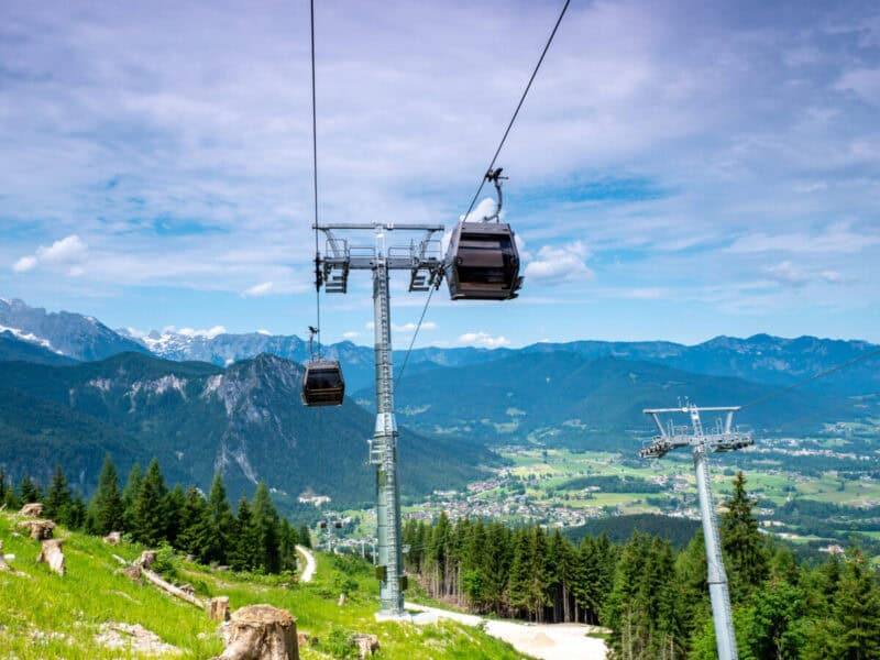 Jennerbahn cable cars gliding over pine forests with a sweeping view of Berchtesgaden valley and distant snow peaks.