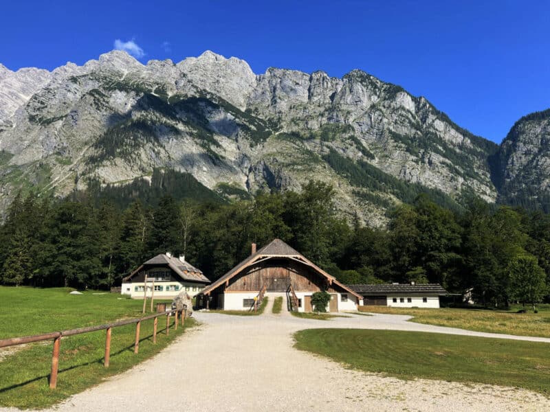 Wooden alpine huts at Königssee with dramatic grey cliffs and forested slopes rising in the background on a sunny day