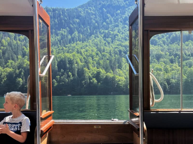 A child seated inside the boat as the open doors frame a scenic view of the lake and forest-covered hills at Königssee.