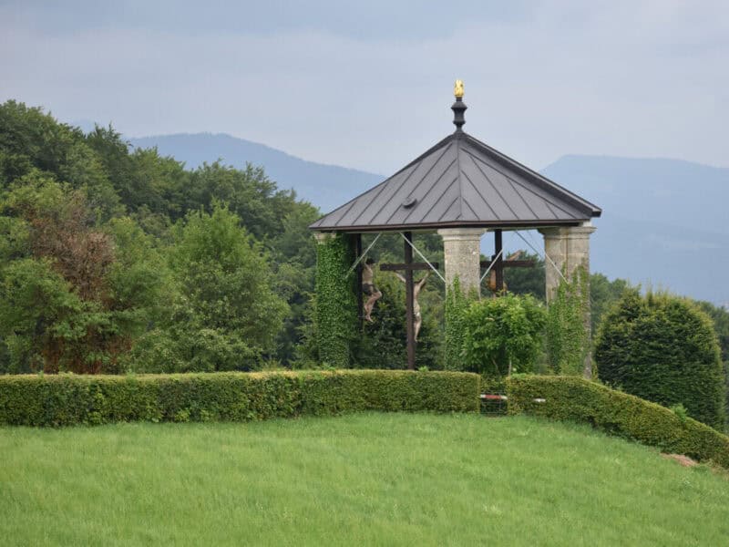 Outdoor crucifixion shrine covered in ivy with three wooden crosses under a pointed roof