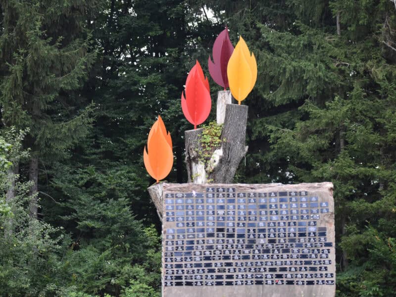 Memorial wall at Paxnatura burial site with colourful flame-shaped markers and black name plaques