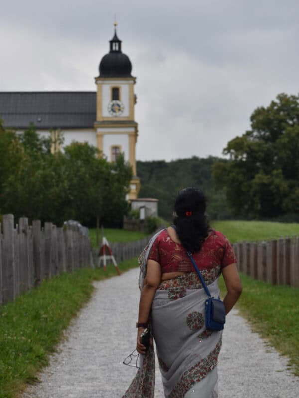 Woman in saree walking towards Maria Plain church along a gravel path on a cloudy day