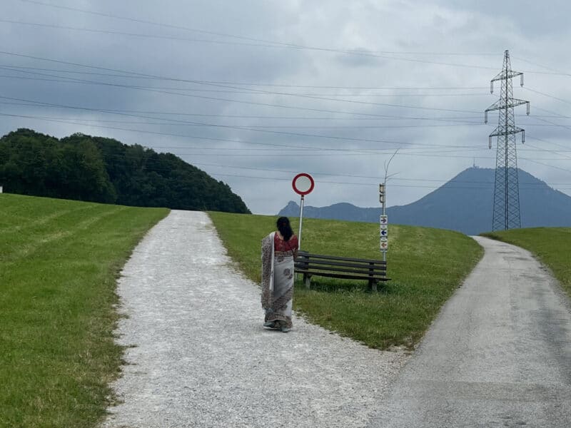 Woman in saree walking past a red circle sign at a fork on the Maria Plain hiking trail near Salzburg