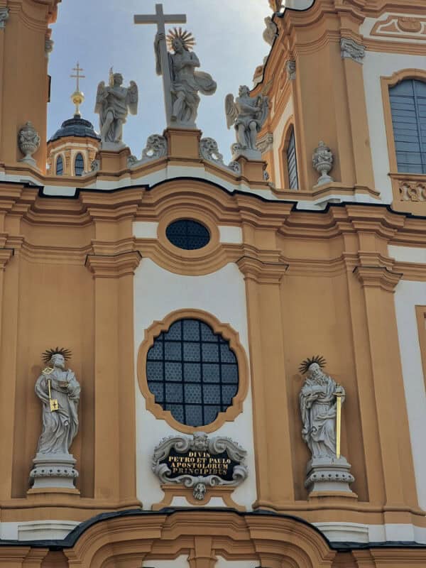 Close-up of Melk Abbey’s yellow and white facade with baroque statues of saints and angels, including a central figure holding a cross above an arched window.