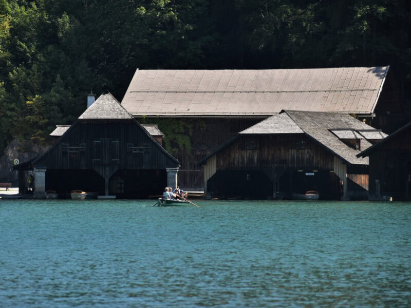 Traditional wooden boathouses on Königssee with a small rowboat and people enjoying the lake view nearby