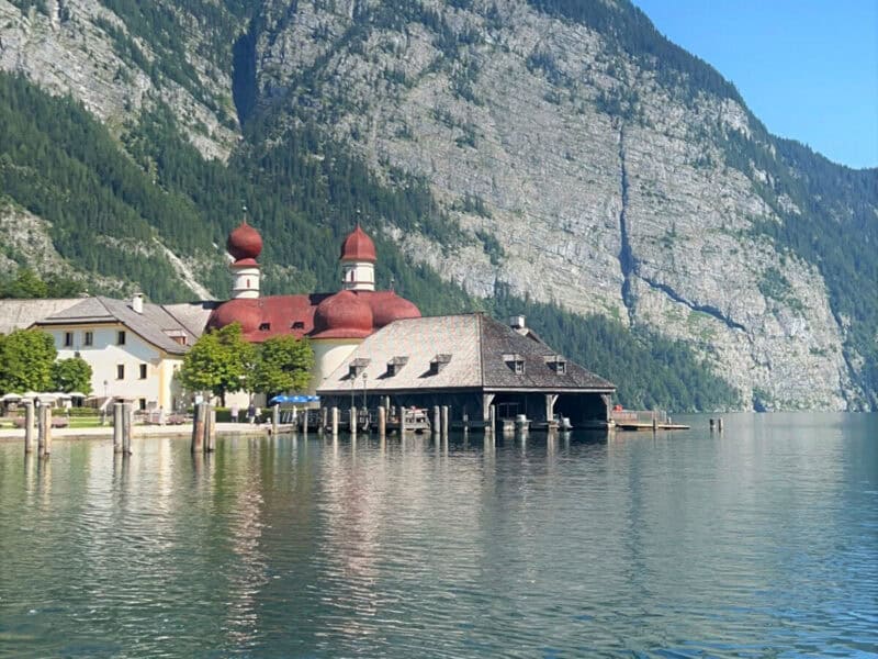 St. Bartholomä church with red domes reflected on Königssee, backed by dramatic alpine cliffs and the Watzmann peaks.