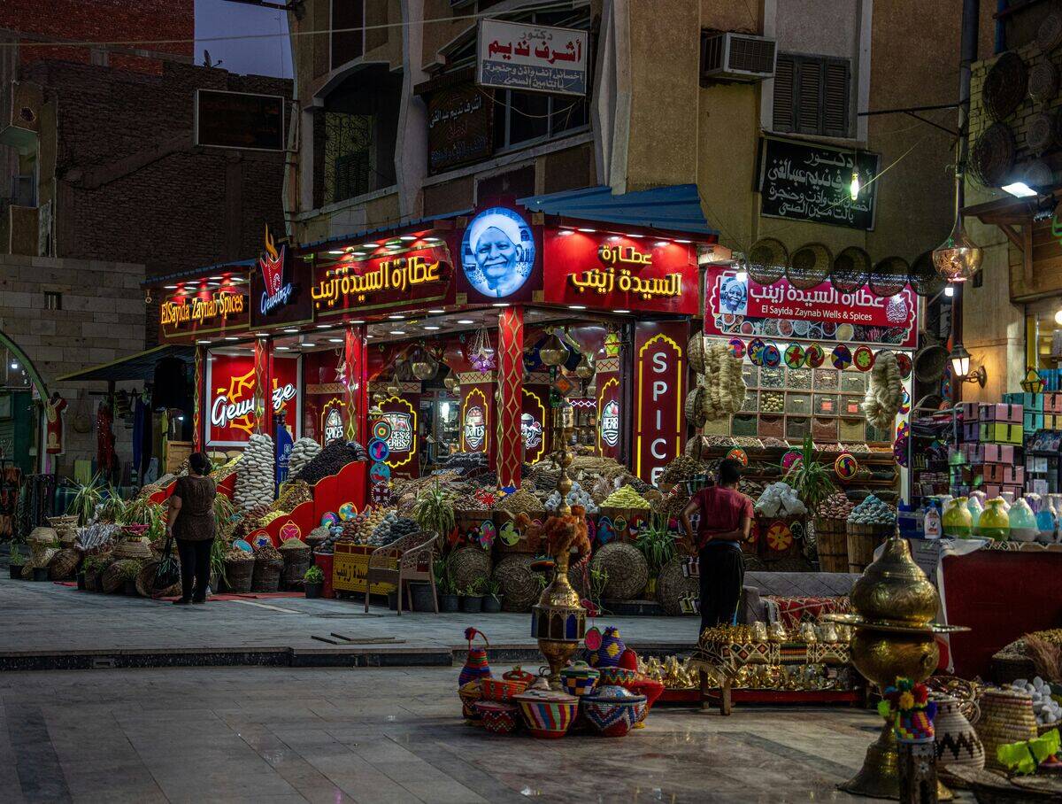 Spice and herb shop in Aswan lit at night with bright red signs, baskets of spices displayed outside.