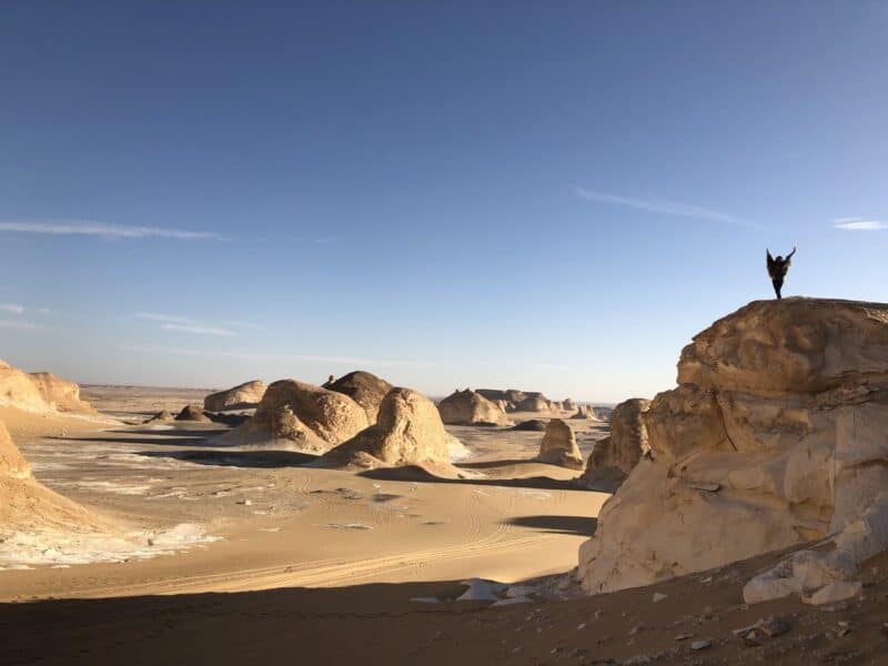 Traveller standing on a rock in the White Desert, Egypt with limestone formations in the background.