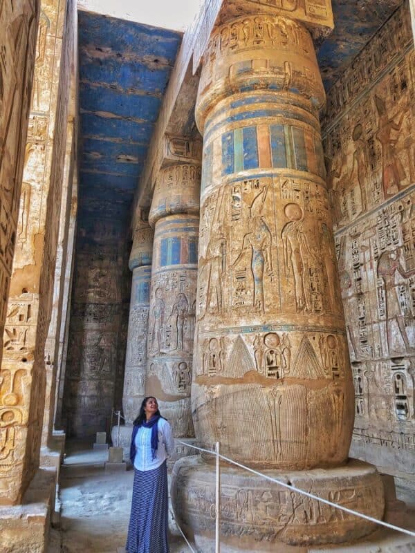 Tourist standing under decorated columns with colourful carvings at Medinet Habu