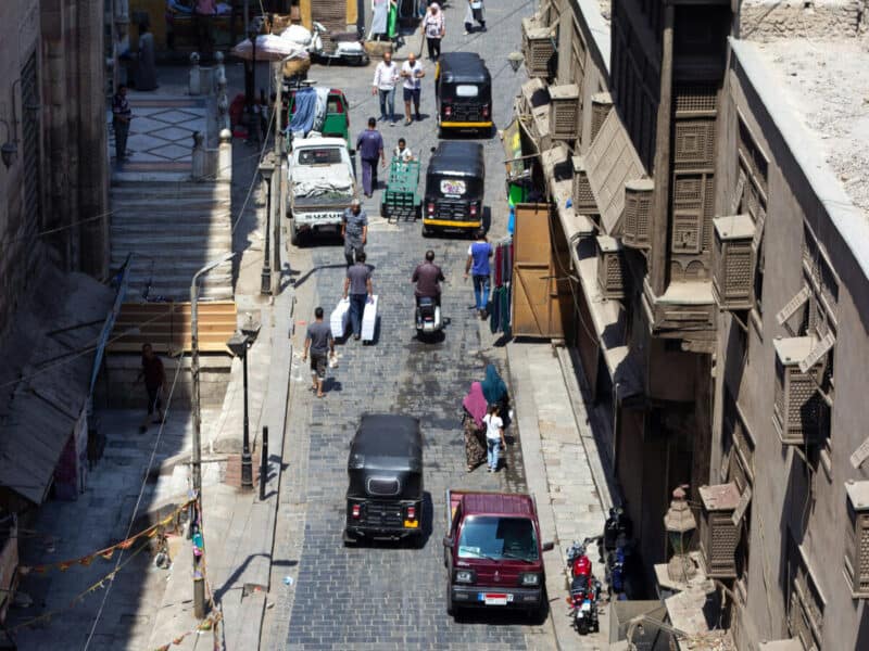 View from above of tuk-tuks, scooters, and people on a narrow street in Old Cairo, Egypt.