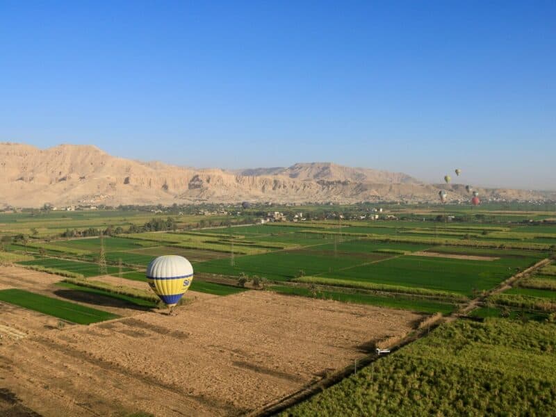 Hot air balloons flying over the fields and mountains of Luxor, Egypt.
