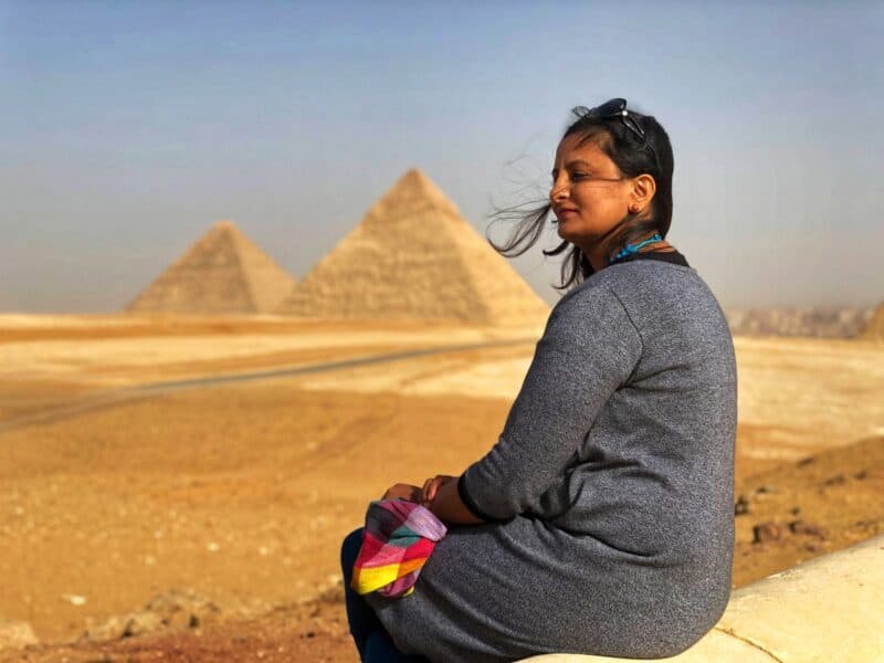 Woman sitting with the Pyramids of Giza in the background, Egypt.