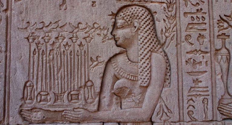 Ancient Egyptian wall carving showing a detailed figure with hieroglyphs and floral motifs on temple stone wall