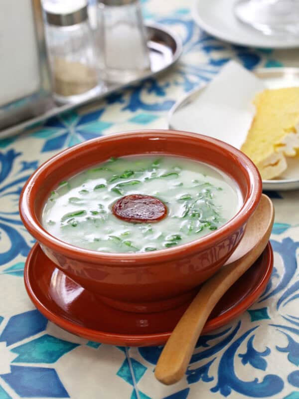 Traditional caldo verde soup with greens and chouriço slice served in a clay bowl on a tiled table in Portugal.