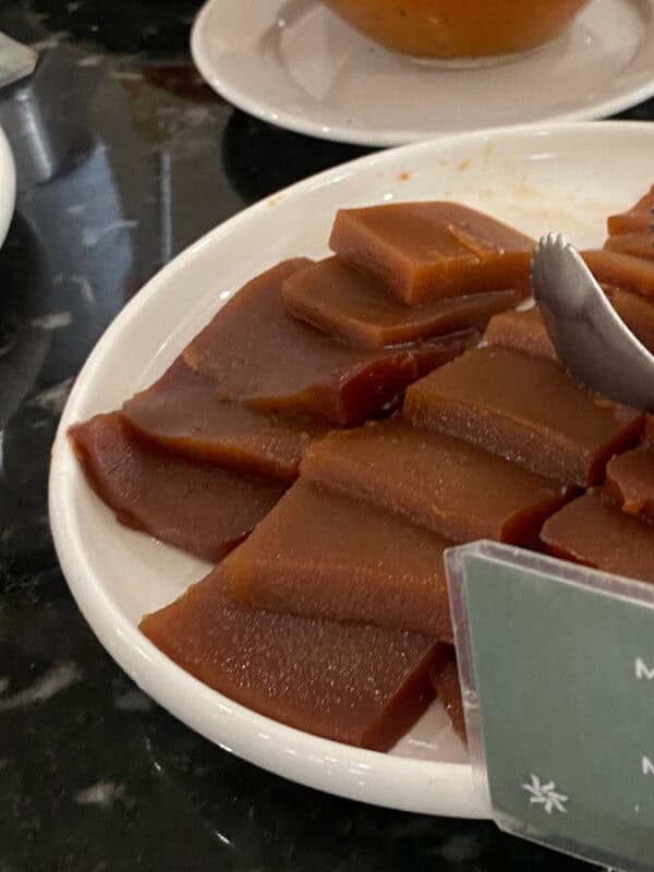 Slices of dark caramelised marmelada jam served on a white plate at a Portuguese buffet counter.