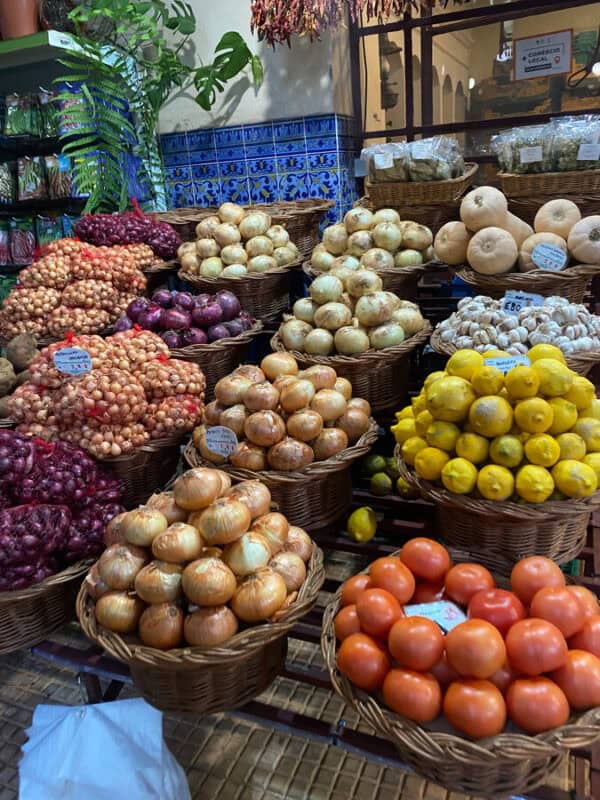 Baskets of onions, lemons, tomatoes and garlic stacked at a traditional food market in funchal , Portugal, with blue tiled walls.
