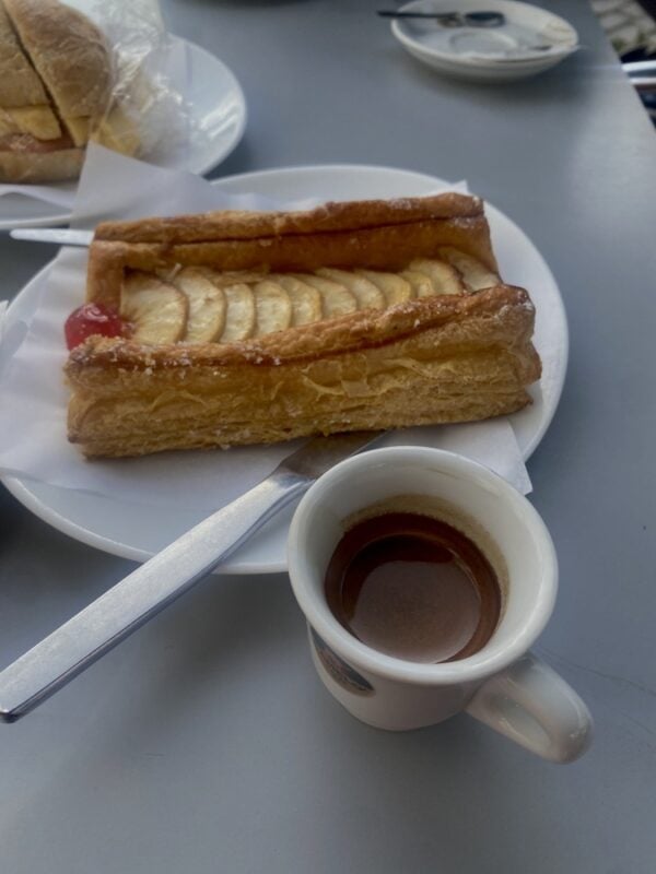 Rectangular puff pastry with sliced apple served with an espresso on a café table in Portugal.