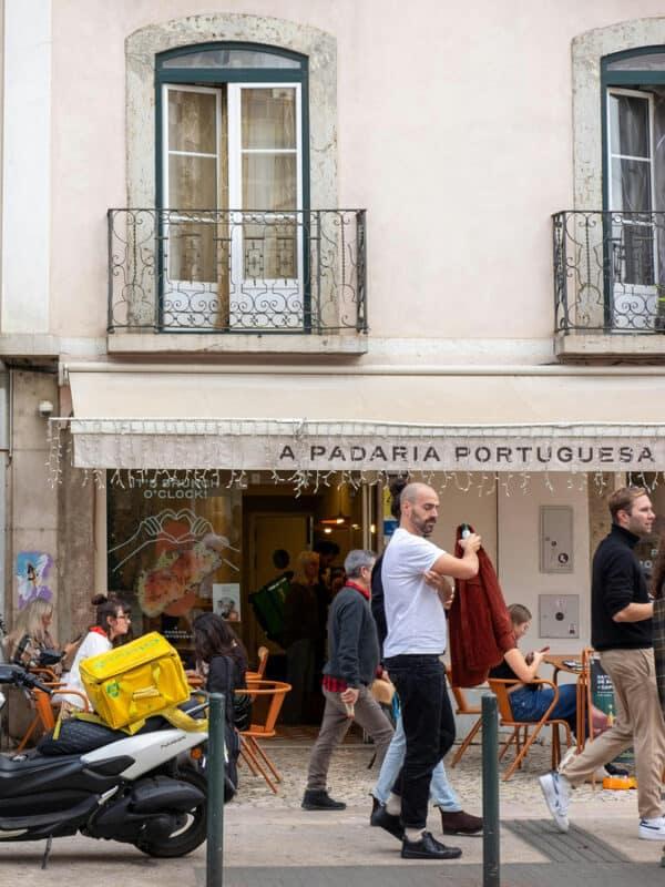 Exterior of a busy Lisbon bakery café with people seated outside and pastries visible inside.