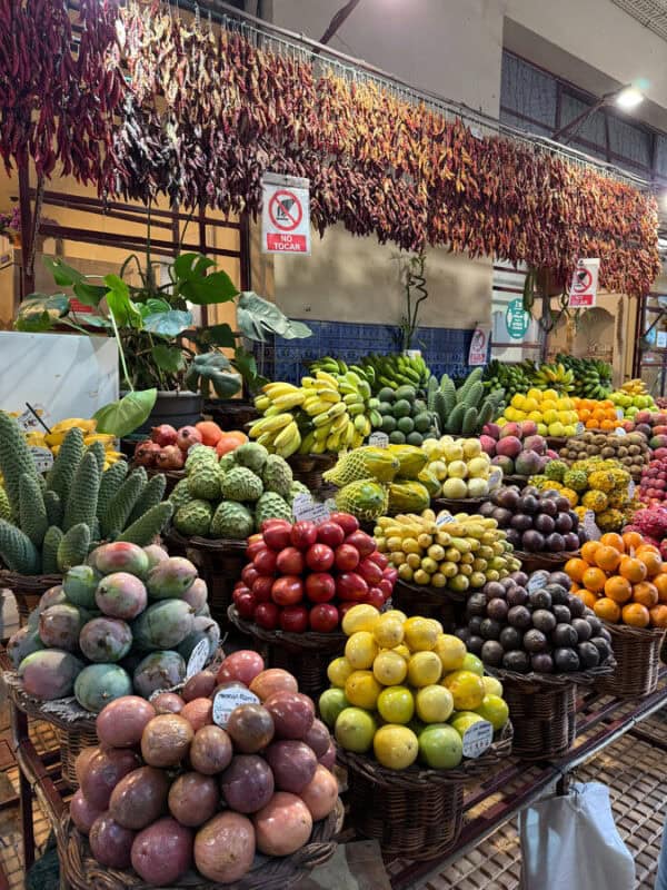 Colourful fruit baskets stacked at Mercado dos Lavradores in Funchal, Portugal, with dried chillies hanging above the stall.