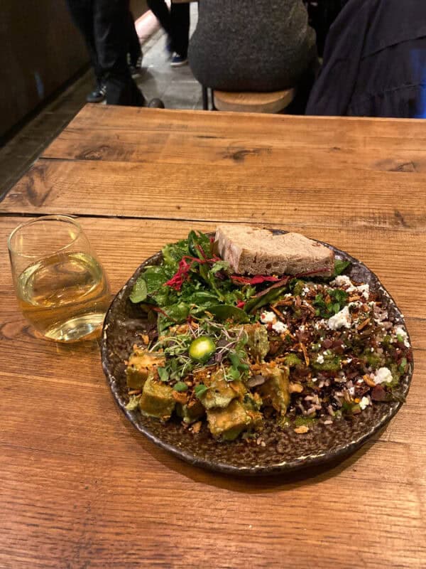Plate of mixed vegetarian food with salad, grains and bread served at a honest greens restaurant in Porto, Portugal, on a wooden table.