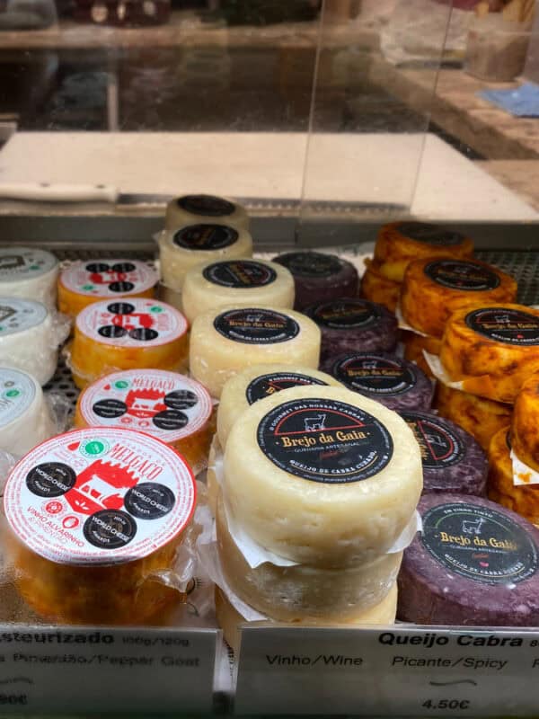 Assorted Portuguese cheeses stacked in a refrigerated market case with price labels and flavour tags.