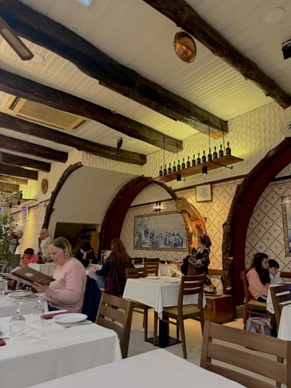 Traditional Portuguese restaurant Centenario  interior with tiled walls, wooden beams and diners seated at white tablecloth tables.