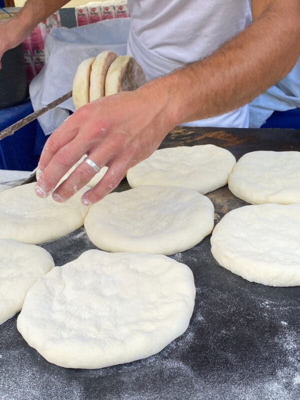 Fresh dough rounds being shaped into bolo do caco by hand on a floured counter at a street food stall in Madeira, Portugal.