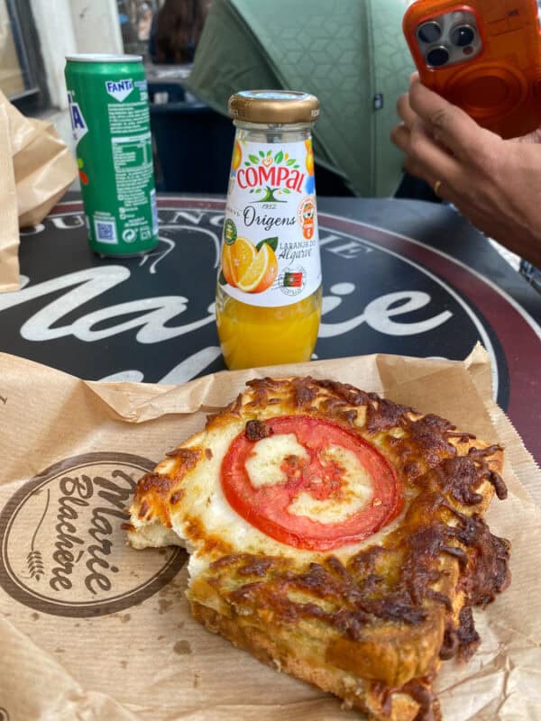 Cheesy toasted sandwich with tomato slice served on bakery paper with bottled orange juice in Portugal.