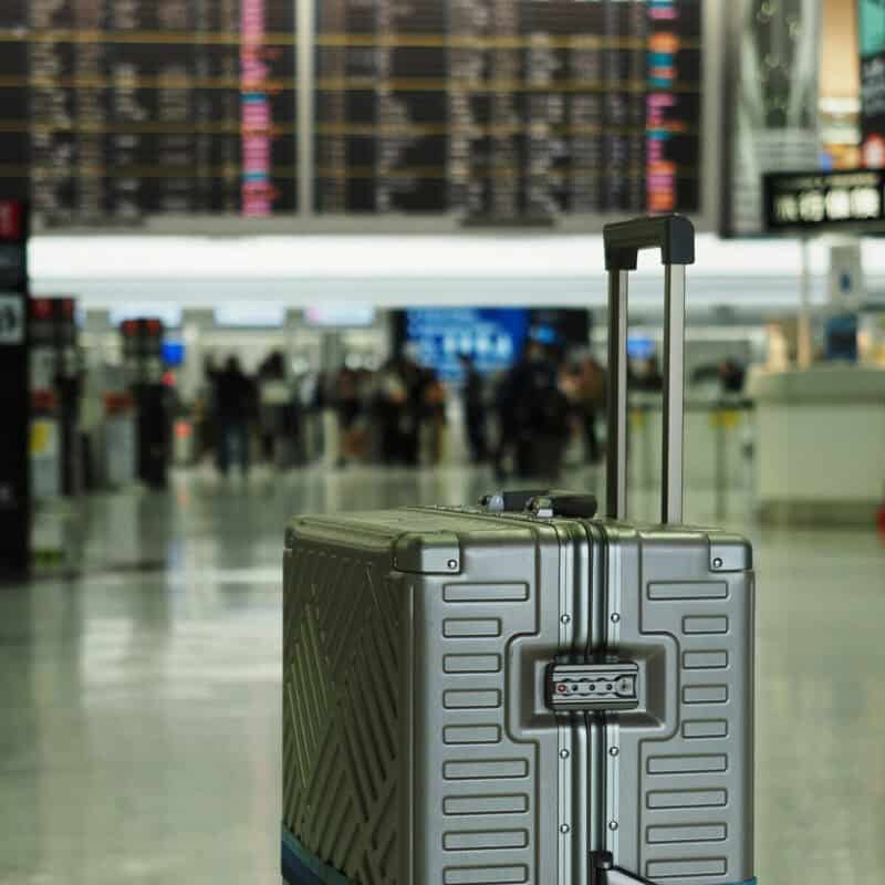 Large suitcase standing inside Lisbon airport terminal with blurred departure board in background