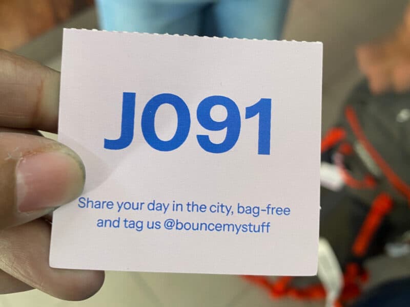 Hand holding Bounce luggage storage receipt ticket in Lisbon with code number printed on it