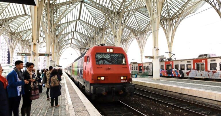 Red train at a modern station in Portugal with travellers waiting on the platform