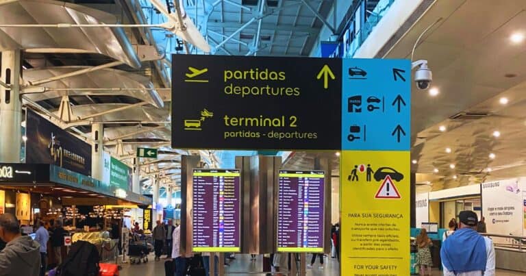 Lisbon Airport departures hall with terminal 2 signboards, flight information screens and travellers moving with luggage