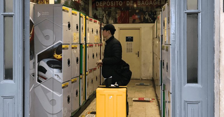 Man standing with a yellow suitcase using luggage storage lockers inside a facility in Lisbon with rows of lockers on both sides