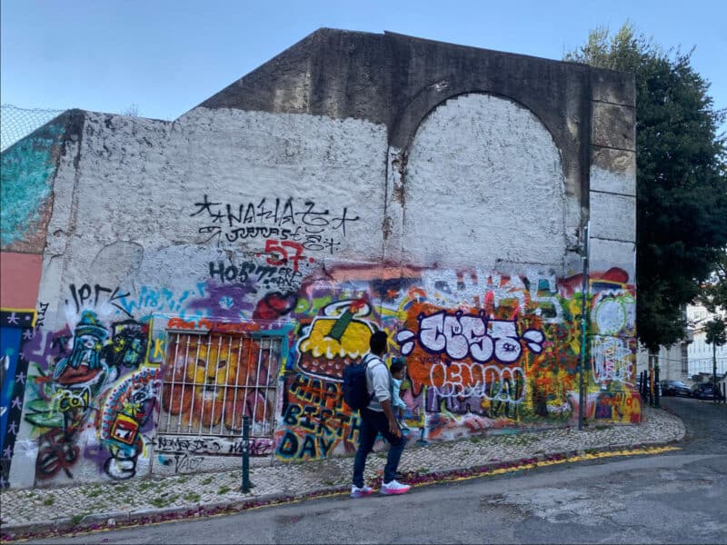 Colourful graffiti wall in Lisbon with a person walking past on a quiet steep street