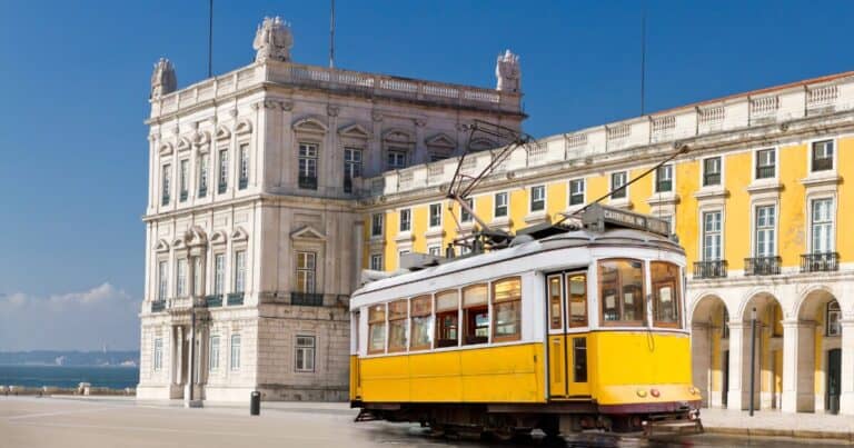 Yellow Lisbon tram near Praça do Comércio with historic buildings and waterfront in the background