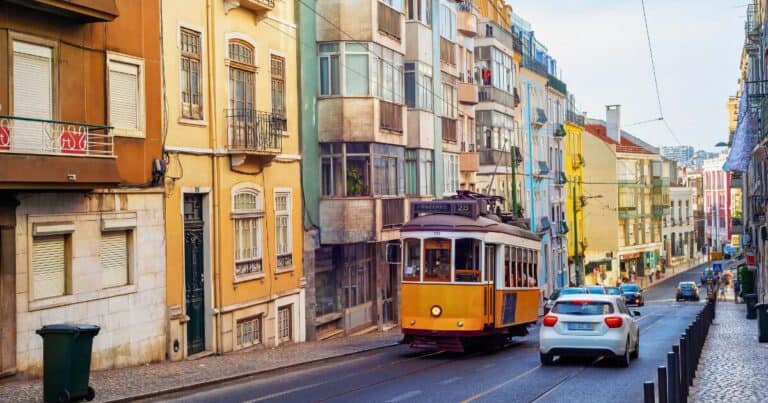 colourful lisbon street with yellow tram moving beside a car and tourists walking