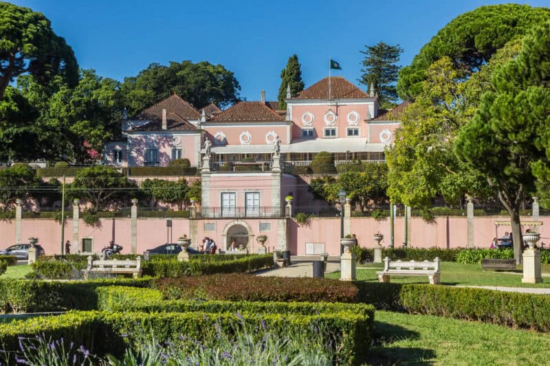 Palácio Nacional de Belém surrounded by manicured gardens and trees on a bright day in Lisbon.