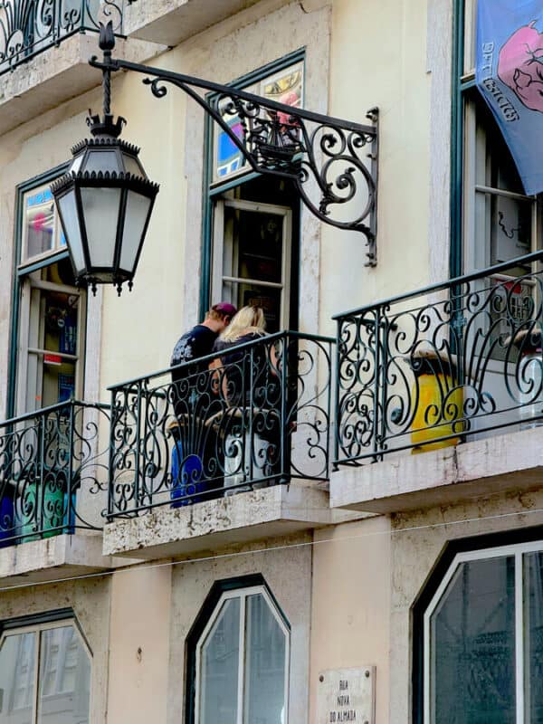 Visitors standing on wrought-iron balconies along Rua Nova do Almada in central Lisbon, surrounded by historic architecture.