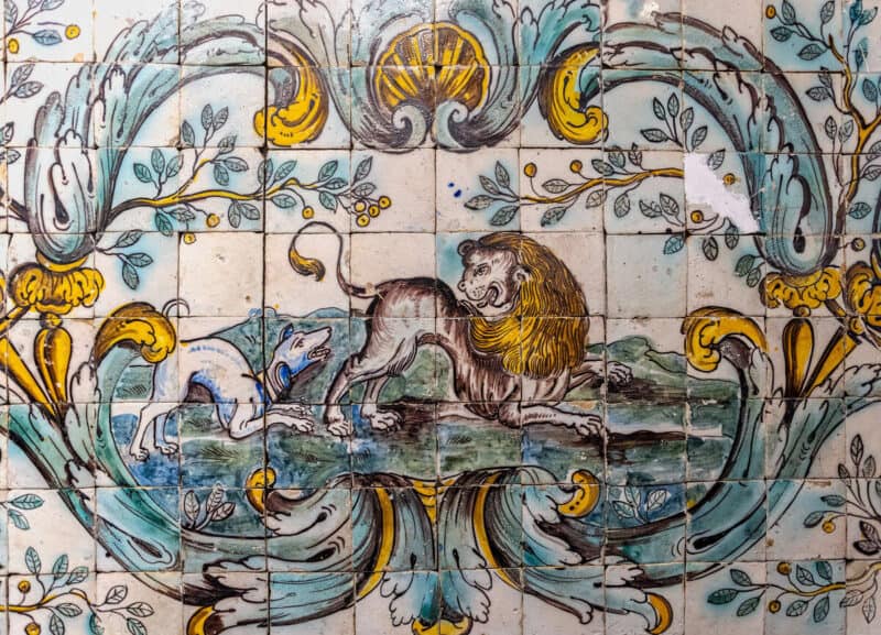 Traditional Portuguese azulejo tile panel featuring decorative floral motifs, a lion, and a dog in historic artwork.