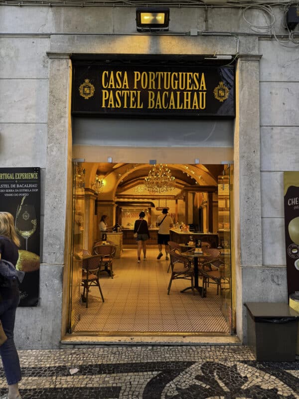 Entrance to Casa Portuguesa do Pastel de Bacalhau in central Lisbon, glowing warmly as visitors step inside from the street.