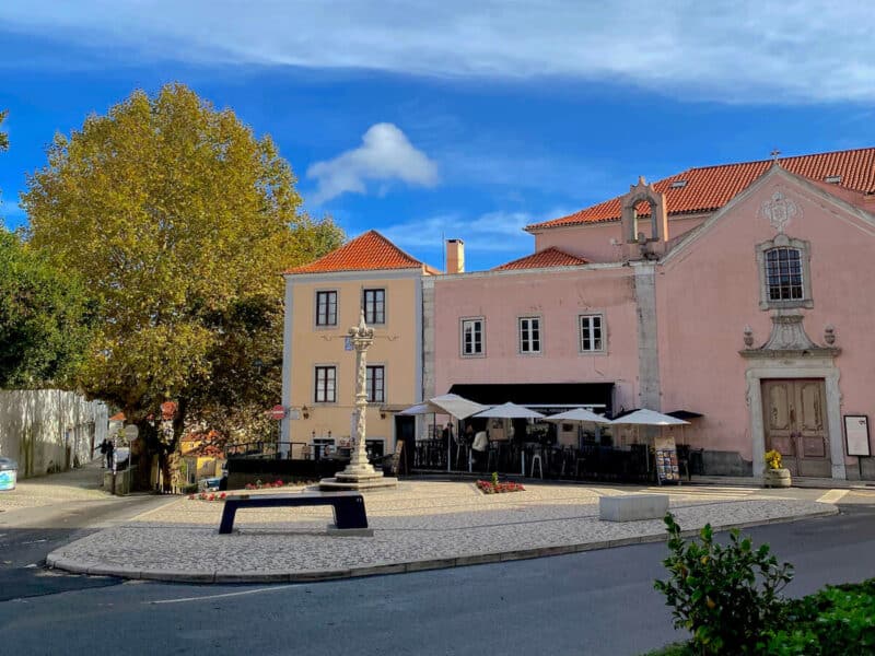 Sintra Historic Centre square beside pedestrian only roads with outdoor cafés, colourful buildings, trees and a clear summer sky.