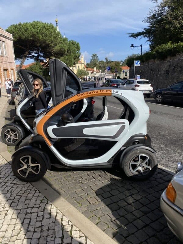Renault Twizy microcars parked beside a Sintra street with a tourist standing nearby