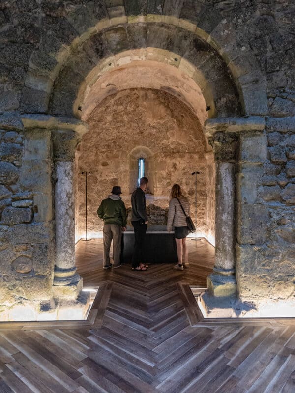 Visitors explore a stone chamber inside a chapel Moorish Castle, with an arched doorway and wooden floor.