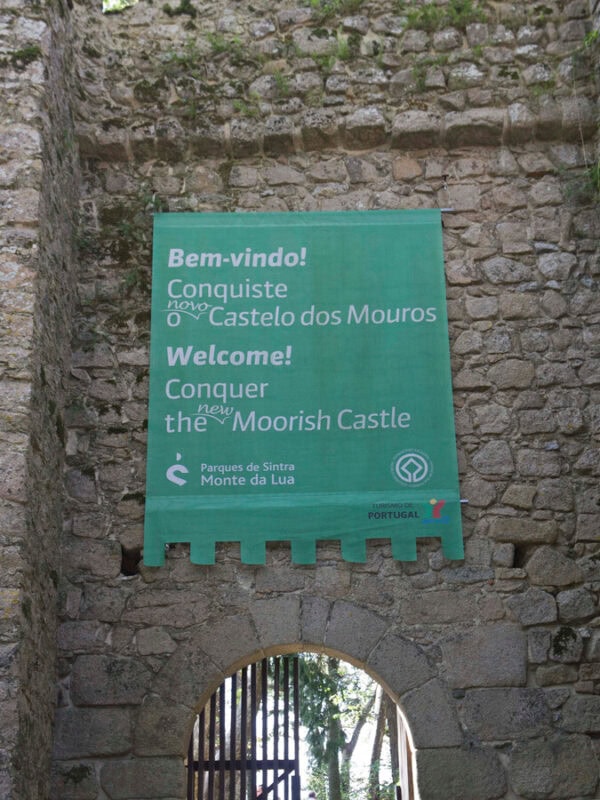 A welcome sign hangs above an entrance gate at Moorish Castle, surrounded by old stone walls.