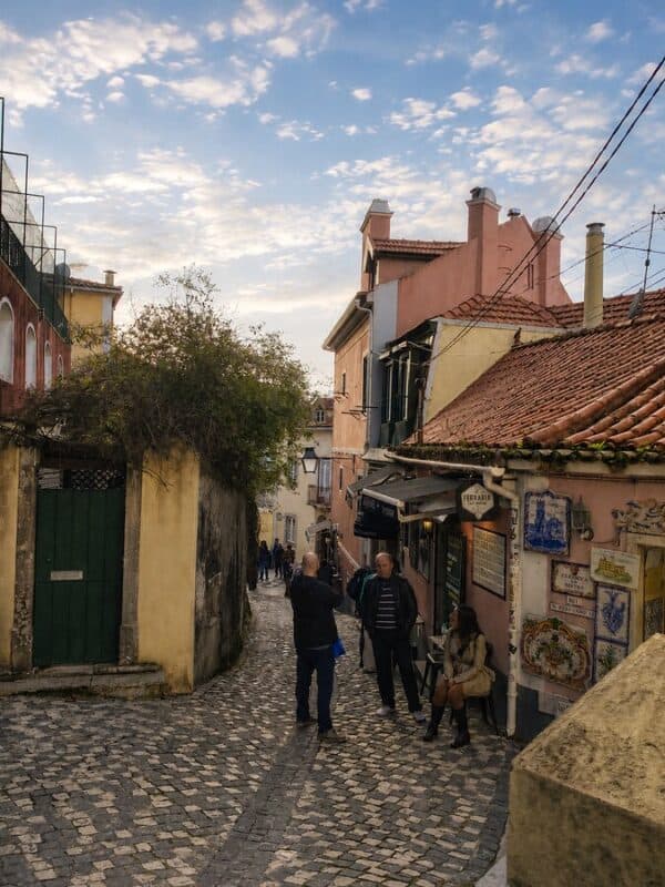 Narrow cobbled street in Sintra lined with colourful historic houses, Portuguese tiles, small shops and people walking downhill.