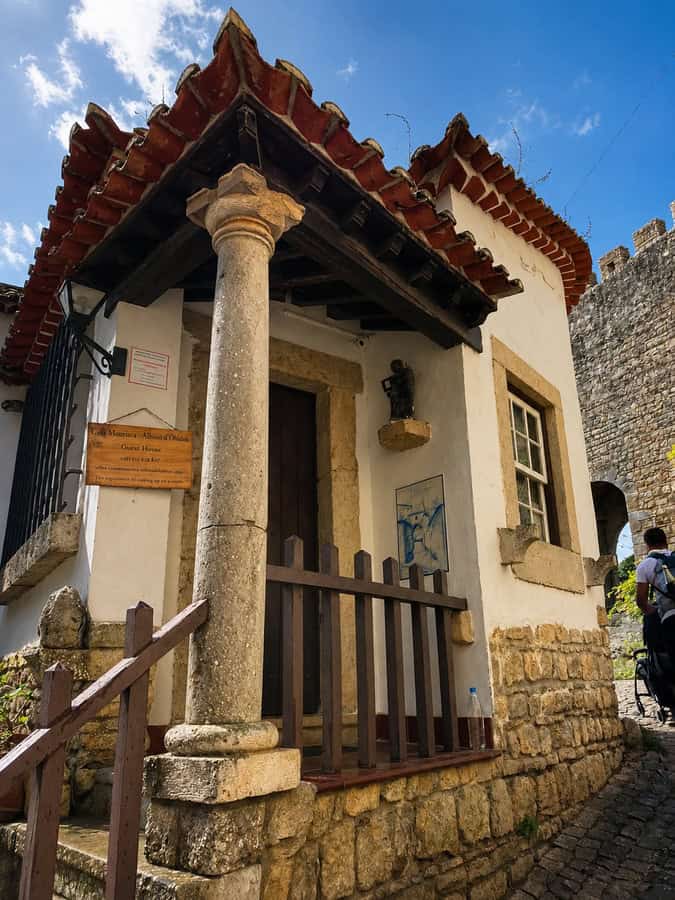 Traditional Óbidos building converted into Casa Mourisca guesthouse, with stone walls beside a cobbled street and the castle wall in the background.