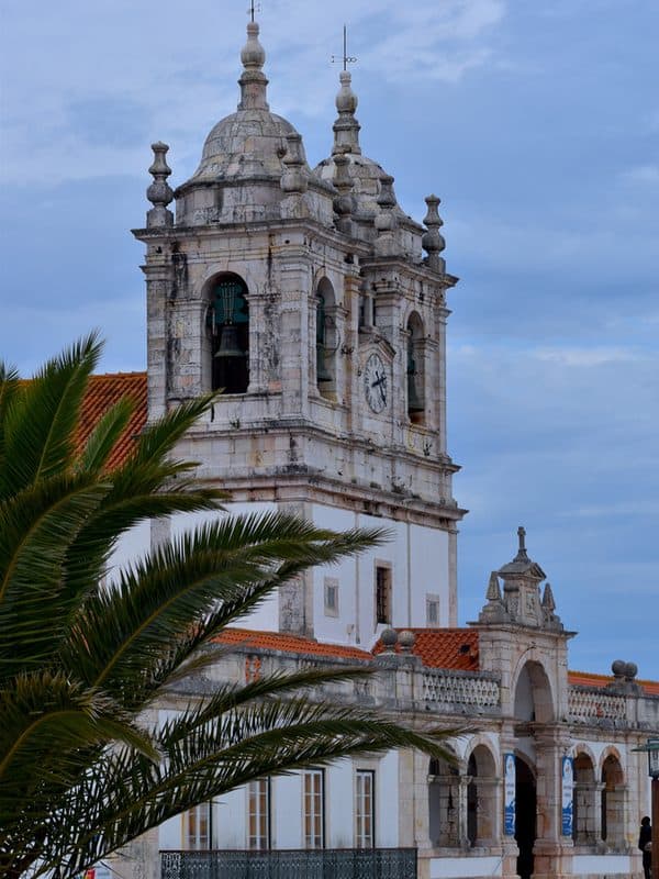 Sanctuary of Our Lady of Nazaré with stone bell towers and an ornate white facade viewed from the front